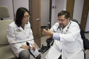 Washington University physician Michael Bavlsik, MD, shows surgeon Ida Fox, MD, how he can now grip an otoscope, which he uses in his practice. He is one of nine quadriplegic patients who regained some hand and arm movement after nerve-transfer surgery, a procedure pioneered at Washington University School of Medicine. Fox, an assistant professor of surgery, operated on Bavlsik. Courtesy: Science Daily 
