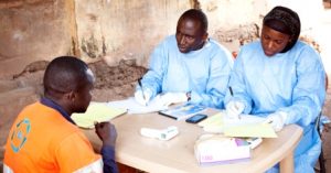 Souare Sekouba (l), and Conde Doussou, (r) part of the WHO vaccine trial teams, run a final follow up with a participant.  Courtesy WHO